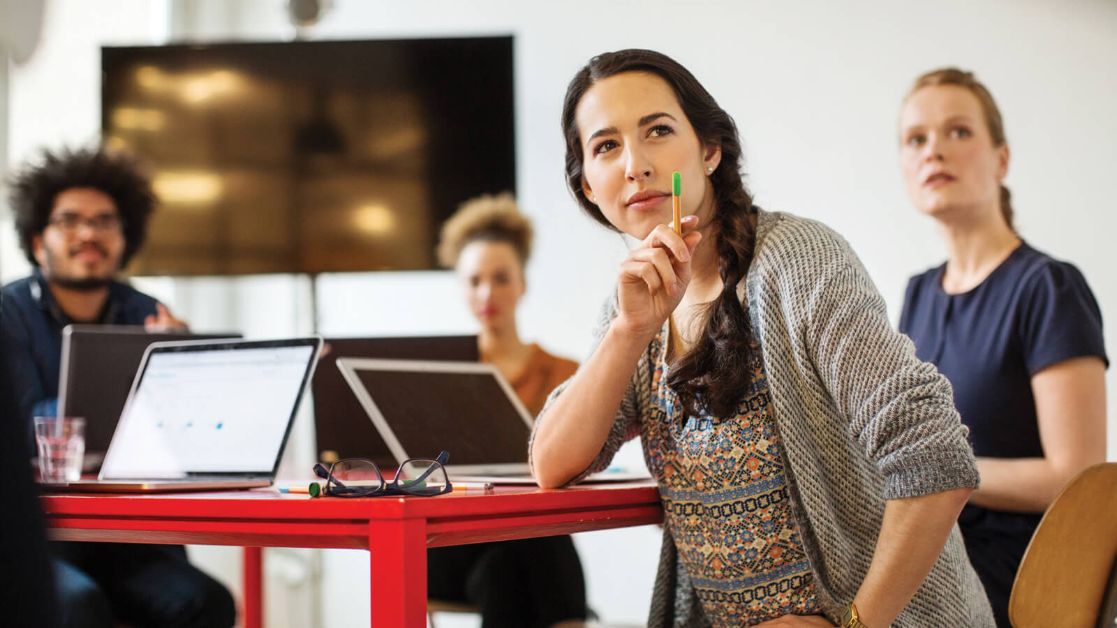 Several work associates with laptops sitting at a table in an office setting.
