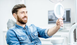 Man with beard smiling looking in mirror while sitting in dental chair.