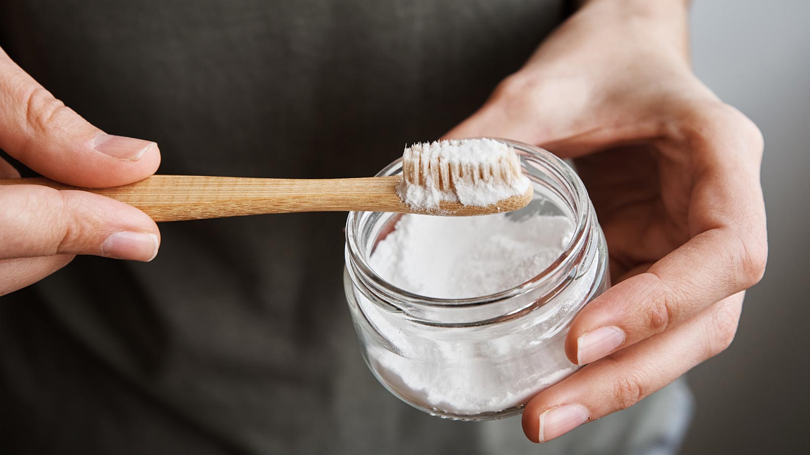 Individual holding a jar of baking soda and a toothbrush.