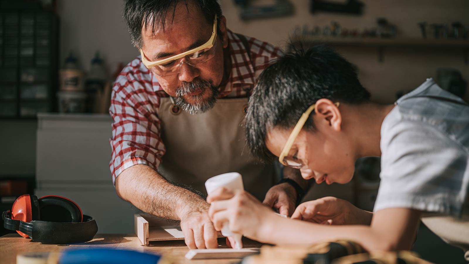 Father and son gluing wood project while wearing safety glasses.