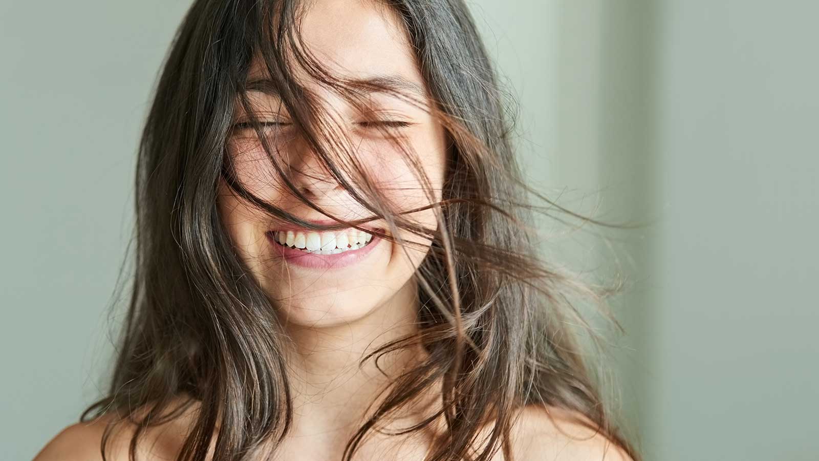 Girl smiling, showing her teeth with hair in her face.