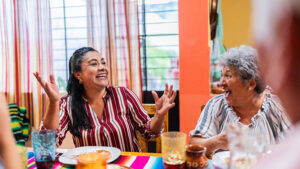 Woman smiling at dinner table with hands in the air.