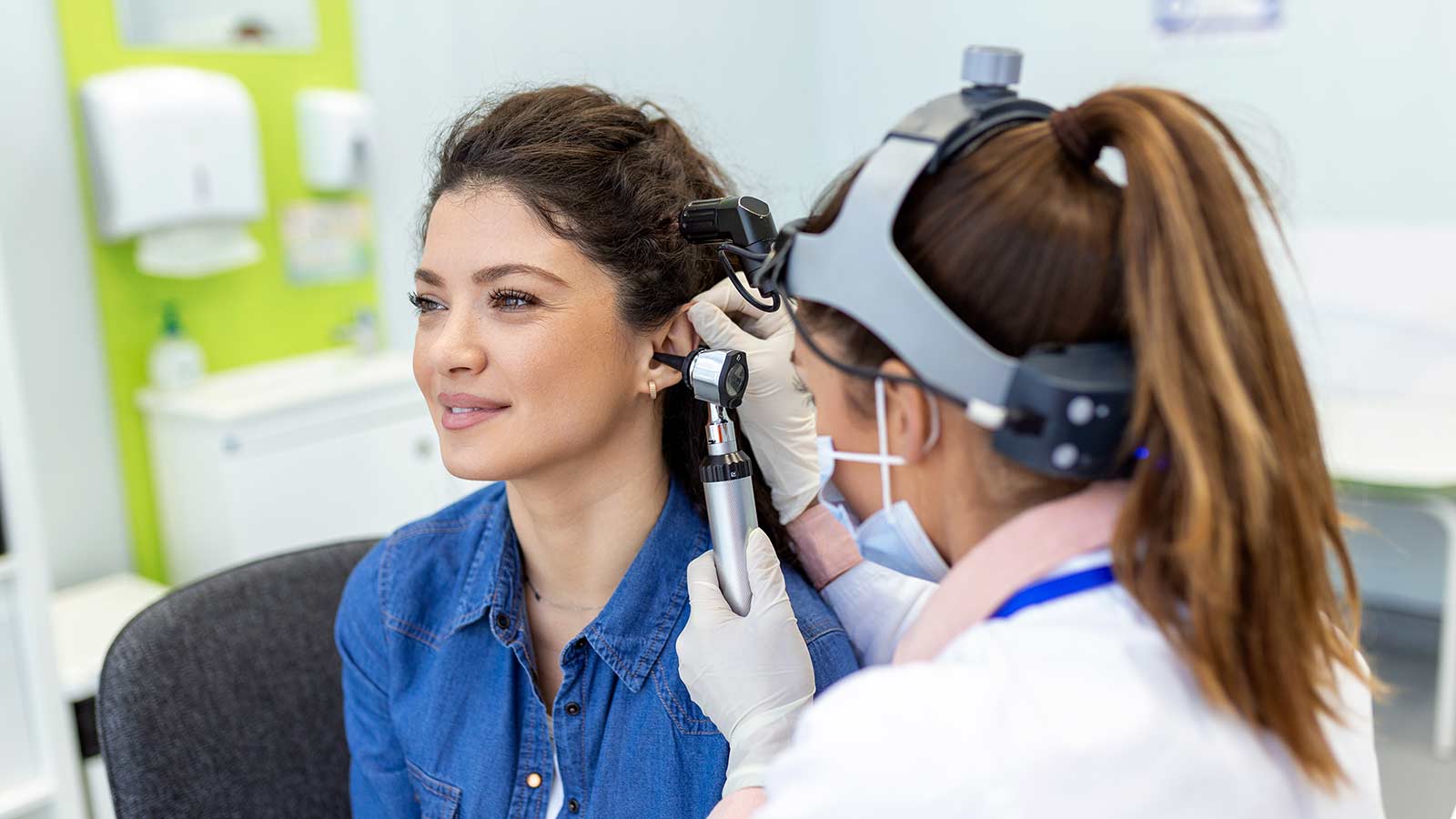 Eye doctor checking woman's ear using otoscope at medical clinic.