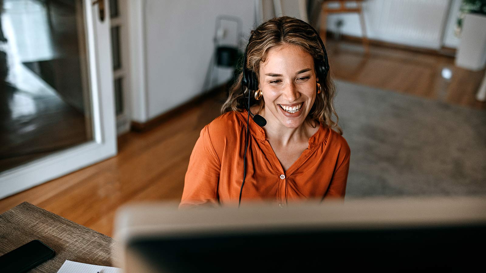 Cheerful young woman video conferencing on computer at home office