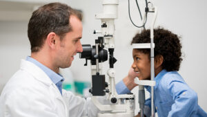 Young child smiling during an eye exam while looking at vision doctor.
