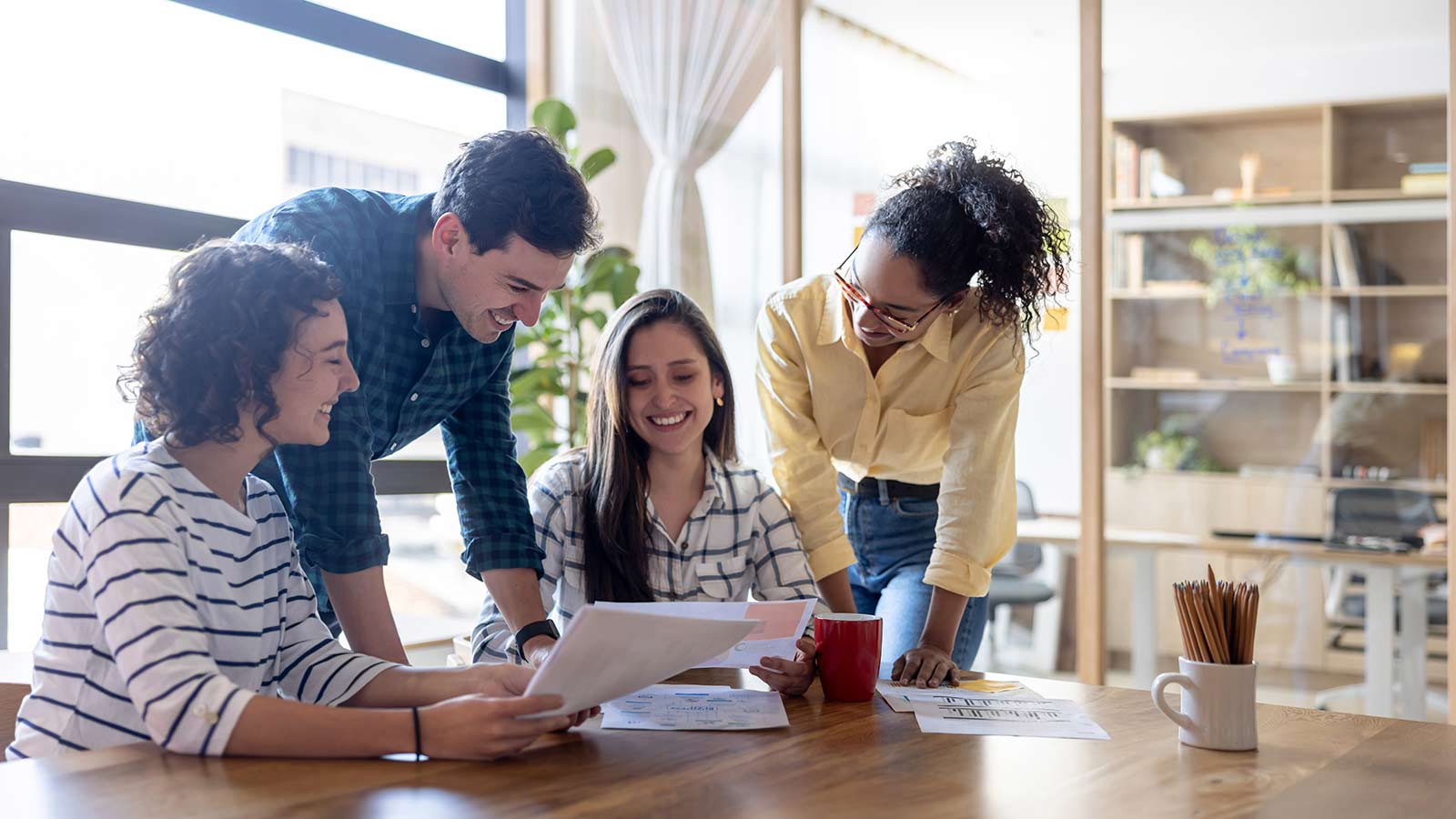 Three colleagues smiling around a table while reviewing paperwork.