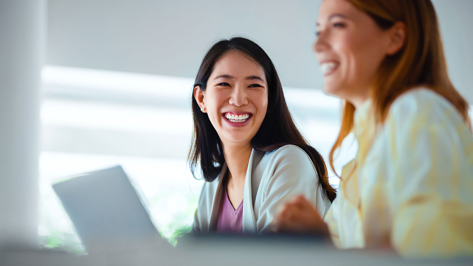 A professional woman in her 30s smiles at her coworker during a meeting in a corporate office.