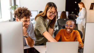Three young professionals sit together in their workplace energetically brainstorming ideas for a project.