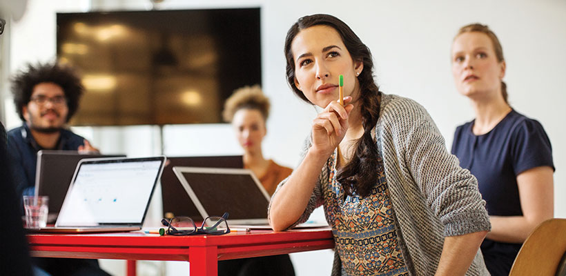 Female standing at desk with laptop looking away.