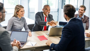 A group of four happy financial professionals sit around a conference table and shake hands with their new RIA representative after business disruption difficulties.