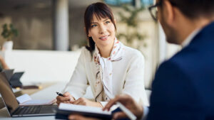 A professional woman working in a corporate office meets with her financial professional to discuss disability insurance to protect her income.