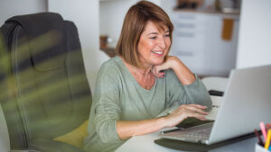 Woman smiling while using laptop on her desk.