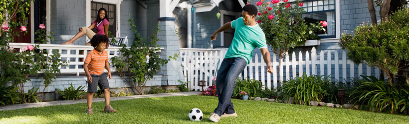 Two brothers kicking a soccer ball on the front lawn of their home.