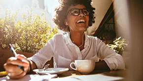 Female enjoying a cup of coffee and working at a table outside.